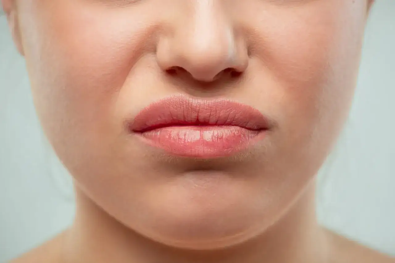 Gros plan sur une bouche pinc&eacute;e, les narines l&eacute;g&egrave;rement pliss&eacute;es. Pourquoi ce nez rouge ? Peut-&ecirc;tre un rhume ou une &eacute;motion forte.