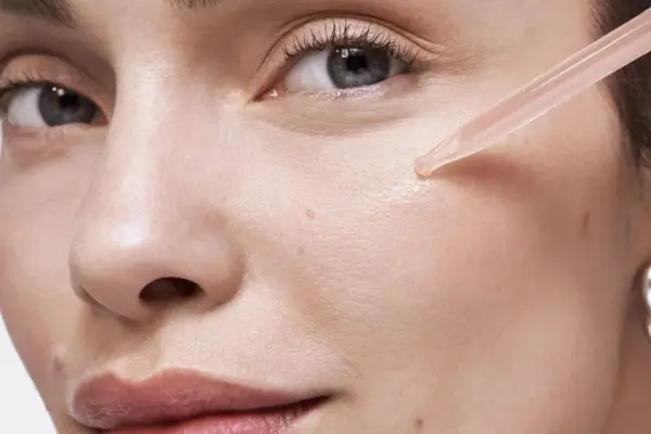 Une pipette dépose une goutte de sérum sur la joue d'une femme. Apprendre comment appliquer un sérum pour une peau éclatante.