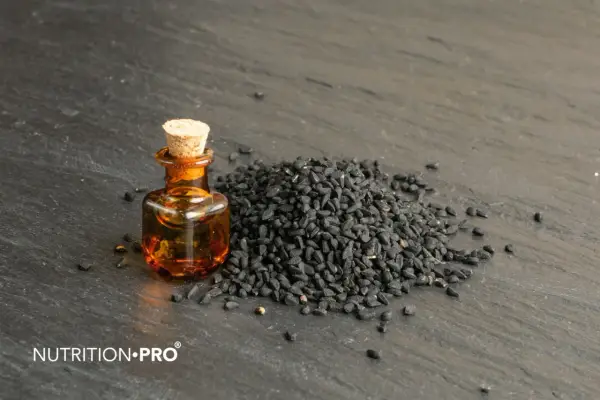 Huile de nigelle dans un flacon, à côté d'une pile de graines noires. Découvrez comment utiliser l'huile de nigelle pour ses bienfaits.