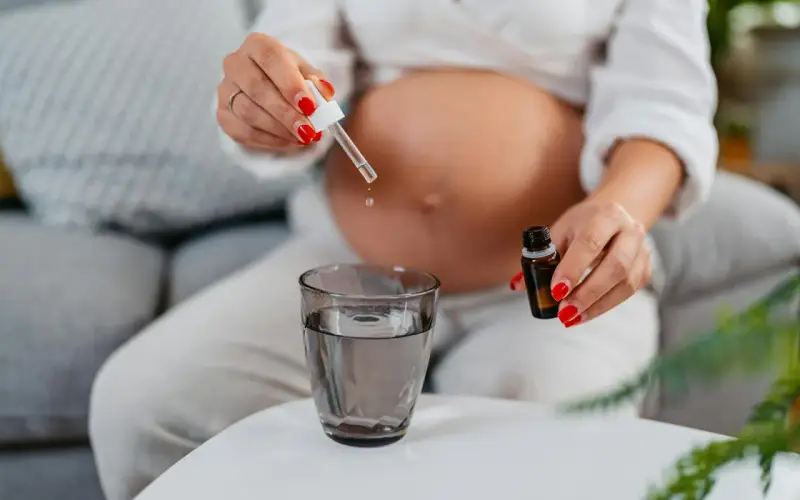 Une femme enceinte ajoute des gouttes d'huile essentielle dans un verre d'eau.